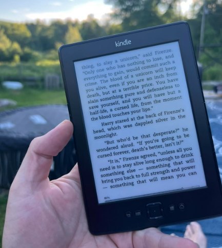 A Kindle showing a page of Harry Potter, held up outdoors