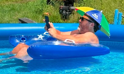 Brian reading on his phone on a pool float, wearing an umbrella hat
